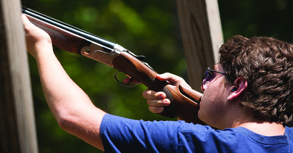 person aiming shotgun to shoot clay target