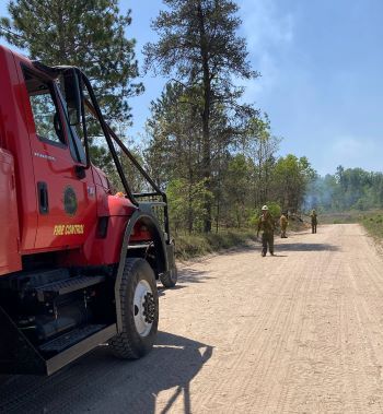 Firefighters and an engine are seen by a roadside near the Wilderness Trail Fire area