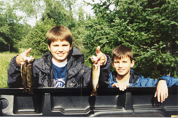 Two young boys with small trout they caught stand near the back of a pickup trout.