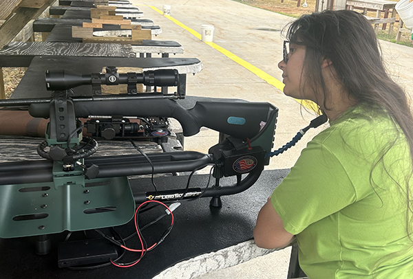 person sitting at shooting range with trigger mechanism on rifle