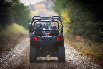 A group of people ride ORVs single file down a wooded trail