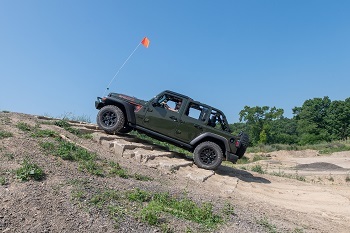 a black, open-top Jeep with an orange flag flying from the front climbs a craggy, rocky area
