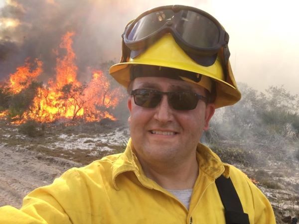 Wildlife biologist Joe Sage takes a selfie in front of flames from a prescribed fire.