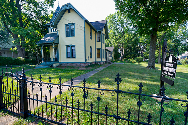 A photo shows the Mann House from outside the wrought iron fencing surrounding the home.