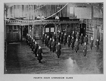 A historic photo shows girls lined up exercising in the school gymnasium.