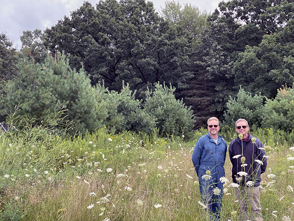 Jim and Steve Simms stand in front of a forest that students planted over the course of 25 years.