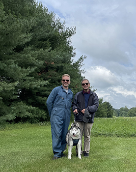 Jim and Steve Simms stand in front of mature trees that students planted in 1998.