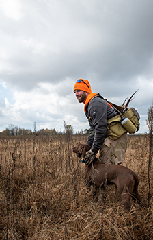 A hunter is shown afield with his dog, both hunting pheasants.