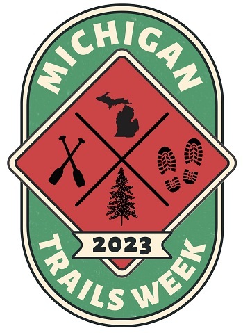 a red and green, oval-shaped graphic for Michigan Trails Week 2023, with icons of footprints, pine trees, Michigan outline and crossed oars