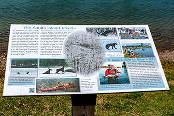 An interpretive display along the St. Marys River discusses the islands of the river at the Soo.
