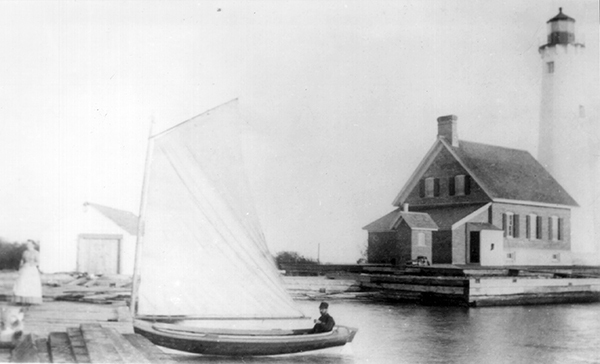 Man in rowboat docks near lighthouse. Woman waits on shore on the photos left.