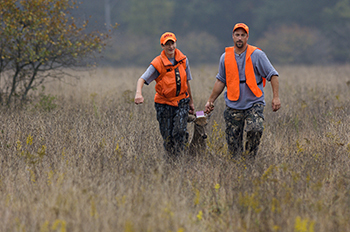 two hunters dragging harvested deer through a field