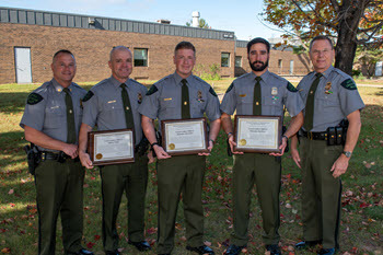 five officers stand  outside posing with award plaques