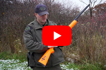 a red video play button overlaid on a man in a gray conservation officer jacket and cap, holding a rifle, standing outside on snowy ground