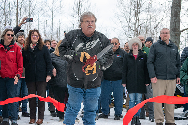 A man faces the camera after cutting a red ribbon celebrating the opening of Trail No. 3 today.