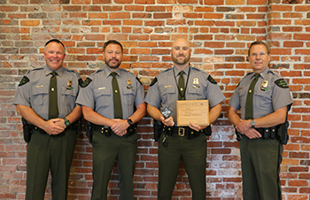 four men smiling, standing at brick wall