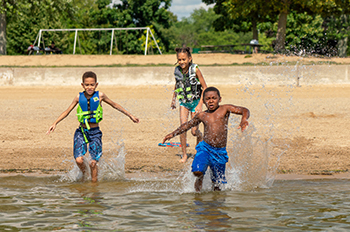 three kids running into water with beach in background