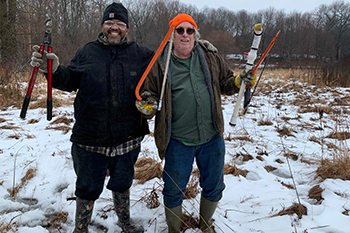 two stewardship volunteers in field holding saw and shrub clippers