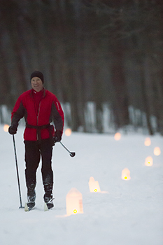 person cross-country skiing along lantern-lit trail