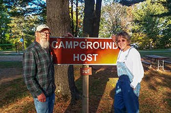 two hosts standing next to campground host sign