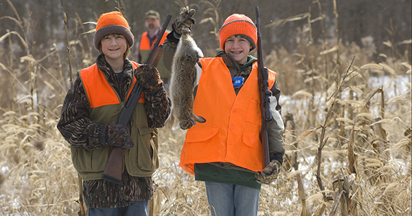 two young hunters in field, one holding up harvested rabbit