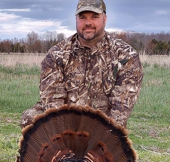 Dennis Tison smiles for camera while holding an eastern wild turkey tail fan.