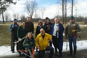 Small group of men and women outdoors, some standing and some kneeling, in winter clothing and holding hacksaws and seed-gathering tubes