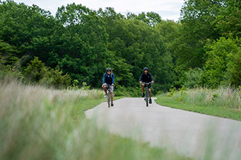 two bikers on paved trail surrounded by trees