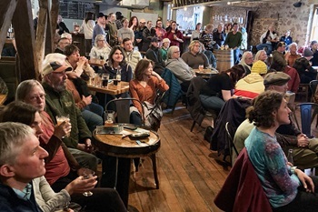 A crowd of people listen to a presentation in a pub.