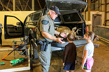 A Michigan DNR conservation officer talks with two young students at a mock crime scene.