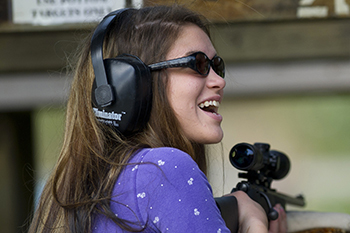 smiling young lady aiming rifle at target