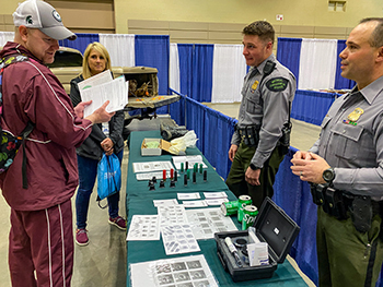 Two Michigan DNR conservation officers talk with a man and woman at an information table.