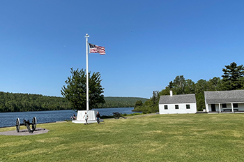 Fort Wilkins buildings, the American flag and cannons over looking the water. 