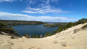 A sweeping sand dune trundles down a slope to a wide, dark lake.