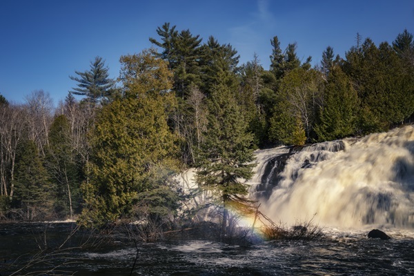 Spring snowmelt at Bond Falls kicks up a fine mist; the sun shining above creates a rainbow amongst the mist. 