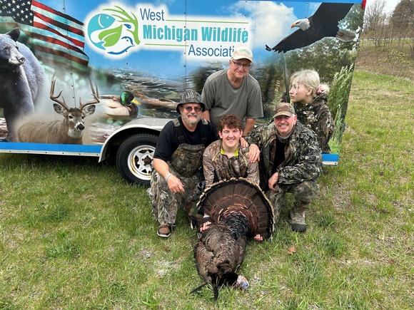 A turkey hunter and his mentor's smile for the camera behind a harvested male turkey with two beards.