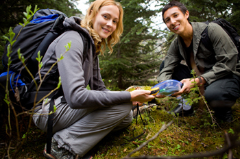 two hikers squatting and holding geocache they found