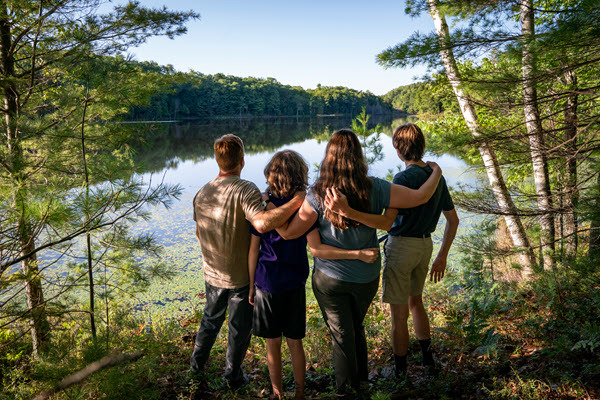 A family of four looks out over a lake with arms on each other's shoulders