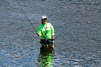 A person wearing bright closing stands in high water, casting a line.