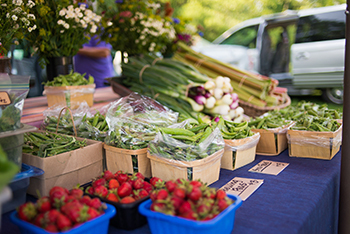 A farmstand overflows with produce in the summer shade.