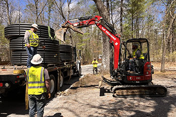 workers in hard hats running lines in campground surrounded by trees