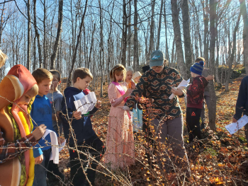 Several Copper Island Academy students look on as an adult shows them invasive autumn olive shrubs in a field.