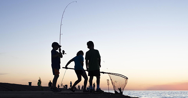 silhouettes of three children on shoreline holding fishing pole and net