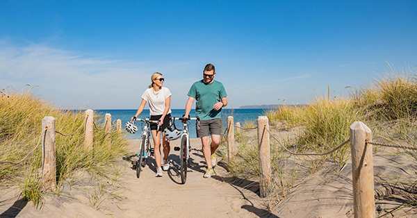 two people walking bikes on sandy dune trail