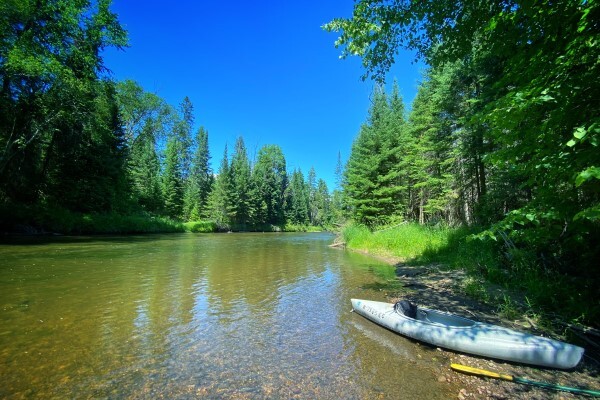 A kayak and paddle rest on a sandbar in the middle of the Rifle River.