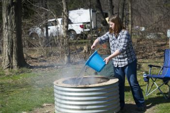 A woman demonstrates the correct way to douse a campfire with water to make sure it is out.