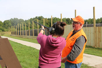 girl shooting firearm with instructor