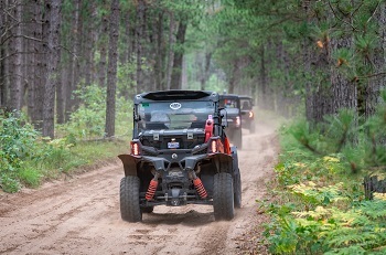 a black off-road vehicle drives down a dirt road in a green, forested area