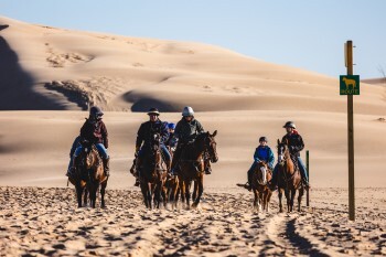 Horses and their riders traverse sunny, sandy shores at Silver Lake.