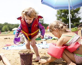 Two children playing in the sand with life jackets